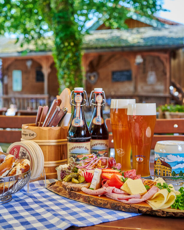 Große Brotzeitplatte auf Tisch in Biergarten, mit Weizengläsern, Brotkorb, Aufstrichen, Käse und Wurst